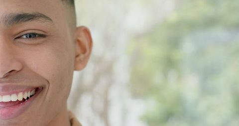 Closeup smiling young man showing teeth with warm expression and soft green natural bokeh