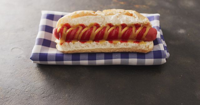 Delicious hot dog served with mustard and ketchup in a fluffy bun, placed on a blue checkered cloth. This makes an appealing visual for fast food industry, recipe books, picnic promotions, or summer cookout advertisements. Great for emphasizing casual dining, family meals, or classic American cuisine.