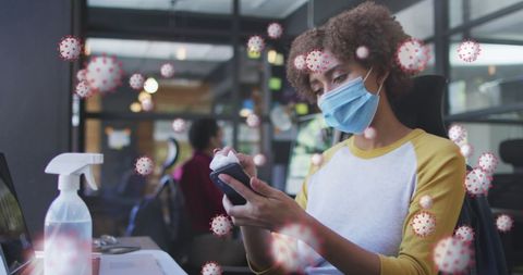 Woman sanitizing smartphone in office with mask