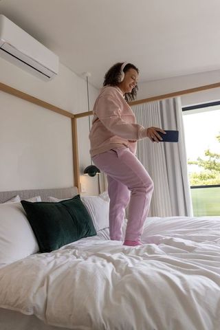 African american woman dancing on bed in modern minimalist bedroom wearing pink loungewear