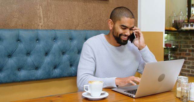 Smiling African American Man Working on Laptop and Talking on Phone in Coffee Shop - Download Free Stock Images Pikwizard.com