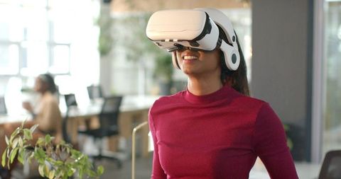 Asian woman experiencing virtual reality headset while coworkers observing in modern office