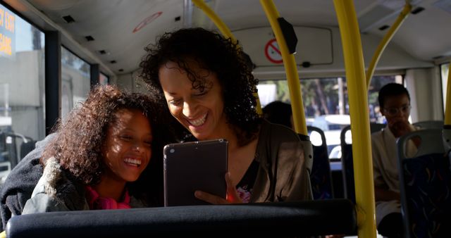 Happy african american mother and daughter sitting in city bus using tablet. Communication, transport, city living and senior lifestyle, unaltered.