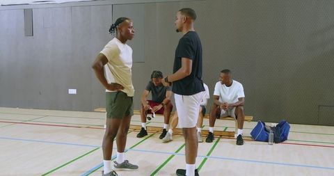 Diverse basketball players discussing strategy and shaking hands on indoor court bench