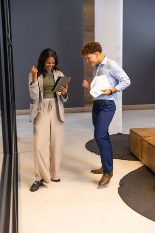 Diverse coworkers celebrating successful project in modern office lobby with tablet