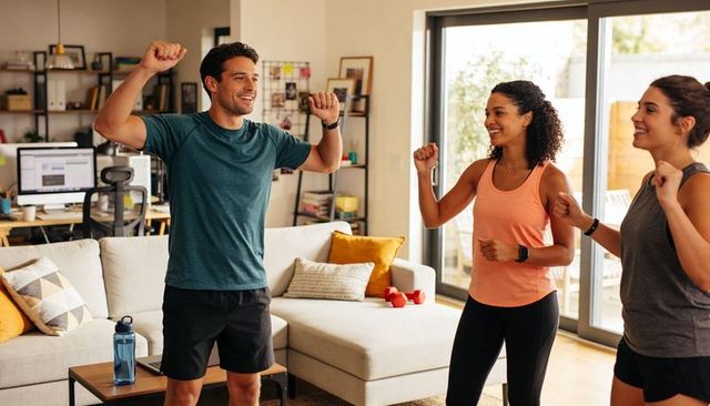Friends exercising at home doing cardio and calisthenics in bright living room with dumbbells
