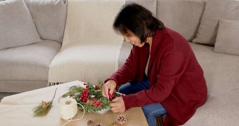 Senior woman crafting holiday wreath in cozy living room