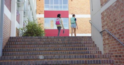 Diverse female friends climbing college campus stairs with backpacks