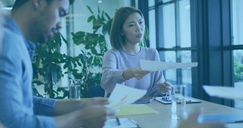 Woman Handing Paper During Team Meeting in Modern Office with Plants and Sunlight