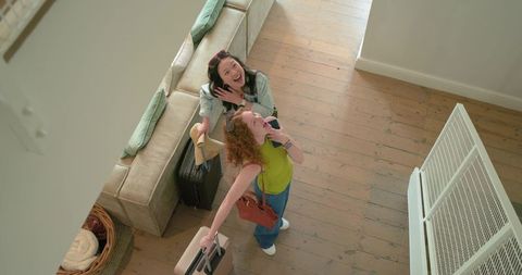 Young women travelers laughing in bright entryway carrying suitcases and checking phone
