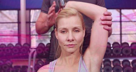 Personal trainer guiding client stretching triceps near dumbbell rack in bright gym