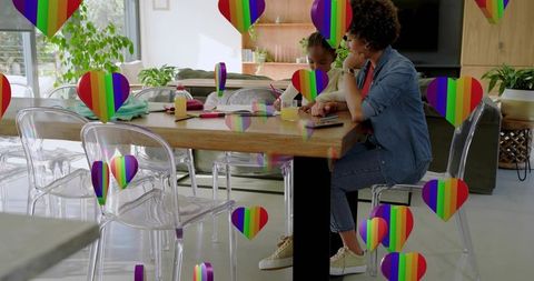 Parent and child sharing tablet at dining table in sunlit home surrounded by rainbow heart icons