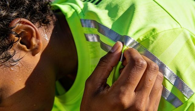 Sunlit closeup of male athlete gripping neon reflective jersey, sweat highlighting fabric