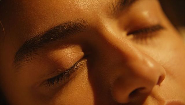 Close-up closed eyes and nose resting in warm golden light revealing skin texture