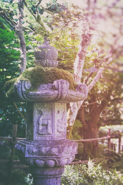 This image features a weathered stone lantern, covered in moss, set in a peaceful garden setting with surrounding lush greenery. It can be used to illustrate themes such as nature, tranquility, and traditional architecture, making it ideal for gardening magazines, travel blogs, and wellness pages aimed at promoting relaxation and ancient cultural elements.