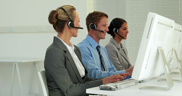 Caucasian and Asian customer service representatives, both male and female, are working at their computers with headsets on. They exemplify a professional team in a modern call center environment, focused on assisting clients.