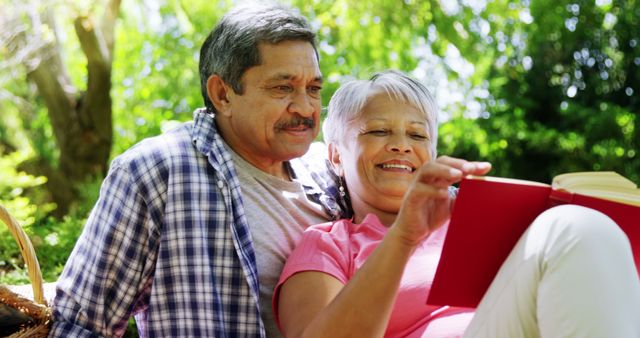 A senior Latino couple enjoys a peaceful moment reading a book together outdoors, with copy space. Their relaxed expressions and the natural setting convey a sense of tranquility and companionship.