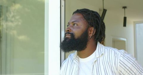 African american man looking upward in sunlit modern entryway striped shirt beard