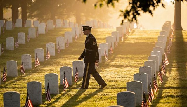 Uniformed honor guard walking among rows of veterans graves with american flags at sunrise