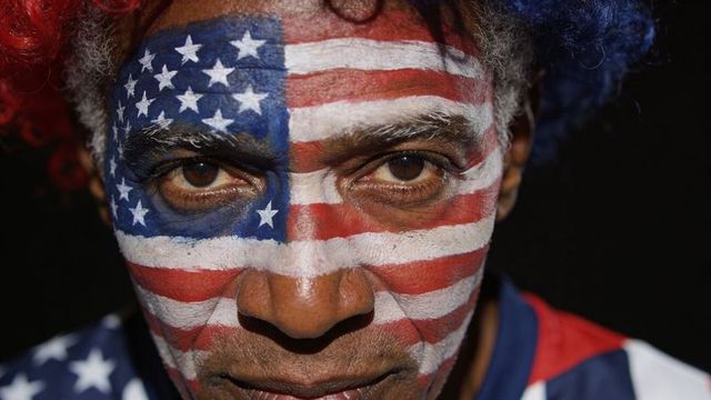 Intense man staring with full-face american flag paint, red-blue wig and patriotic costume