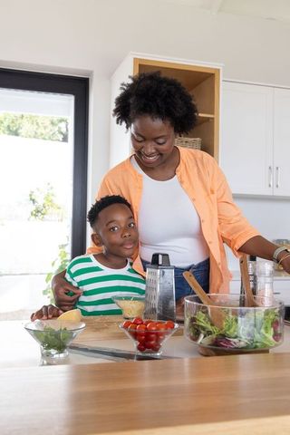 African american mother and son preparing healthy salad together in sunlit kitchen