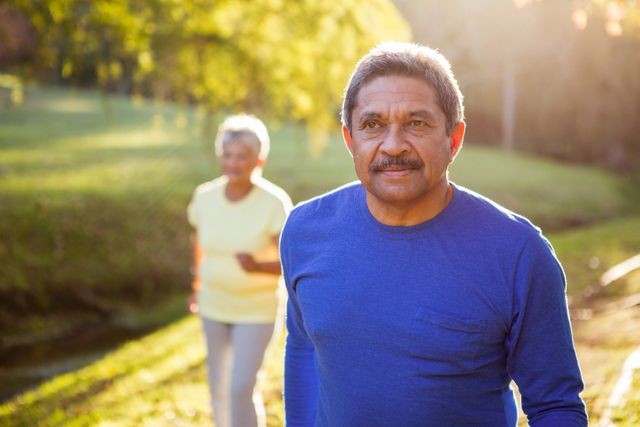 Mature couple enjoying a walk in a sunny park, perfect for promoting healthy lifestyles, senior activities, and outdoor leisure. Ideal for use in health and wellness campaigns, retirement planning materials, and advertisements for outdoor gear or senior services.