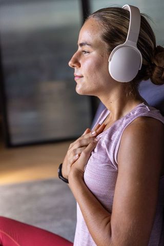 Young woman practicing mindfulness with headphones and heart-centered breath in sunlit room