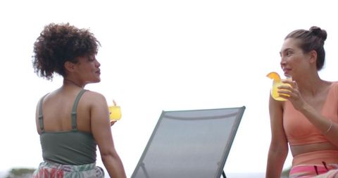 Two women enjoying tropical cocktails on terrace loungers, relaxing summer resort escape