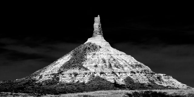 Chimney Rock standing alone under a deep sky. A striking piece of artwork for homes or offices. Useful for projects related to geology, history, and fine art. Familiar landmark provides educational opportunity and cultural interest.