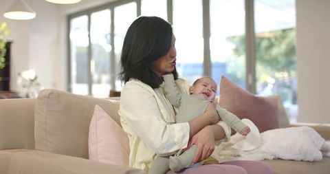 Mother Comforting Infant on Cozy Sofa in Sunlit Living Room