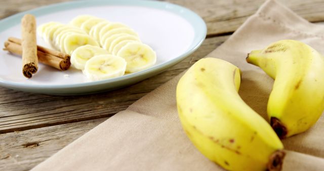 Sliced bananas and cinnamon sticks are arranged on a wooden table, with copy space. Fresh ingredients like these are often used in healthy recipes and baking for natural sweetness and flavor.