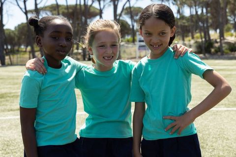 Diverse girls posing on school sports field wearing teal shirts showing teamwork