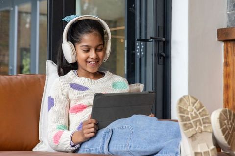 Indian girl relaxing on sofa using tablet with headphones for learning and streaming