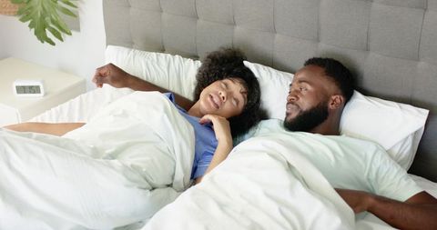 Black couple waking up in bed, woman stretching under white duvet, cozy morning intimacy