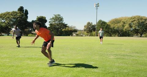 Athletes sprinting on sunlit park field with floodlight pole, teamwork and outdoor fitness