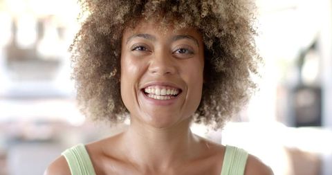 Woman with curly hair smiling in sunlit outdoor scene
