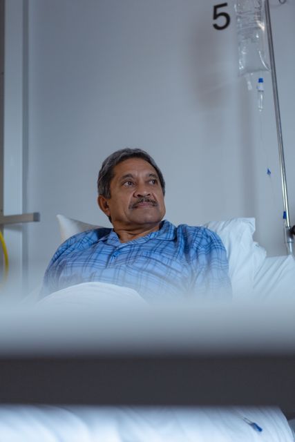 Mature male patient laying on hospital bed, looking relaxed. Ideal for healthcare, medical treatment, recovery, patient care, hospital stay, and health services themes. Can be used in articles, brochures, web content related to healthcare facilities, patient care, and medical treatments.