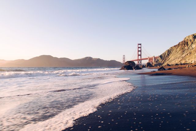 Photo captures the famous Golden Gate Bridge in San Francisco during sunset with waves crashing on the shoreline. Ideal for travel blogs, California tourism promotions, and nature-themed projects showcasing coastal beauty and iconic landmarks.