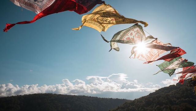 Colorful prayer flags fluttering with sun flare over tree-lined ridge and clear sky