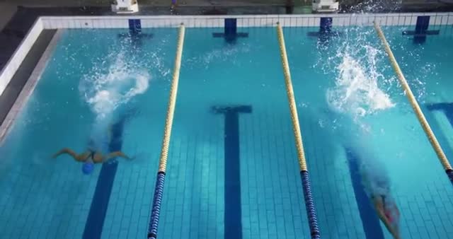 High angle view captures female swimmers in a training session diving into the pool, generating impressive water splashes. Ideal for representing aquatic sports, beginner swimming practice, and showcasing the athletic prowess of female swimmers.