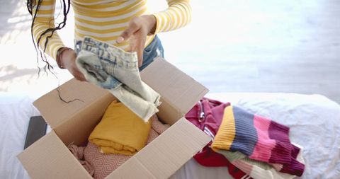 Woman sorting clothes into cardboard box at home