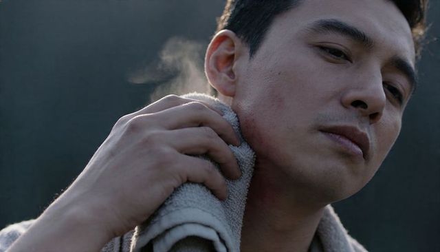 Contemplative asian man pressing towel to neck with rising steam closeup moody portrait
