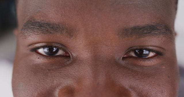 This close-up image shows the eyes of an African American man, capturing the reflection of light in his gaze. Ideal for use in concepts of focus, attention, detail, emotion, and human connection. Perfect for articles and advertisements referring to personal stories, psychological features, or visual details.
