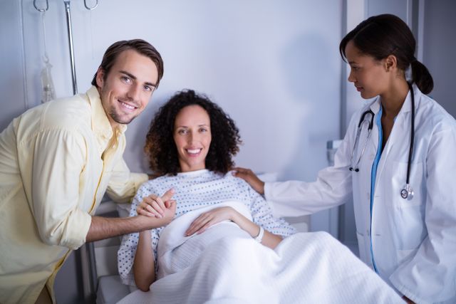 Doctor interacting with pregnant woman and her husband in a hospital room. Ideal for use in medical and healthcare-related content, articles about pregnancy and childbirth, hospital brochures, and promoting family support in prenatal care.