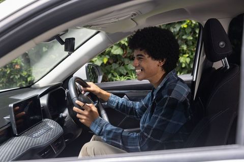 Smiling driver using touchscreen infotainment while holding steering wheel in modern car