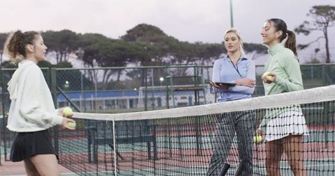 Female tennis coach guiding diverse players during dusk outdoor training session