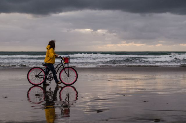 Woman in Yellow Raincoat Walking Bicycle on Beach at Sunset - Download Free Stock Photos Pikwizard.com