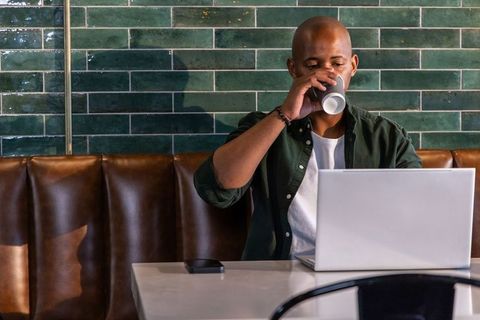 African american man working on laptop and sipping coffee in booth with green tiles