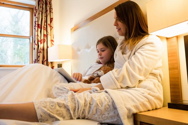 Mother and daughter using digital tablet in bedroom at home