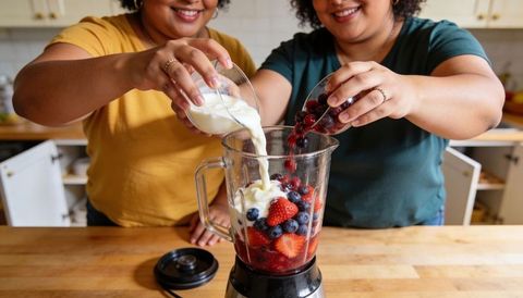 Pouring mixed berry yogurt smoothie together in home kitchen blending healthy breakfast